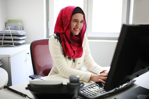 Asian / Malay / Muslim female professional working on computer, smiling.